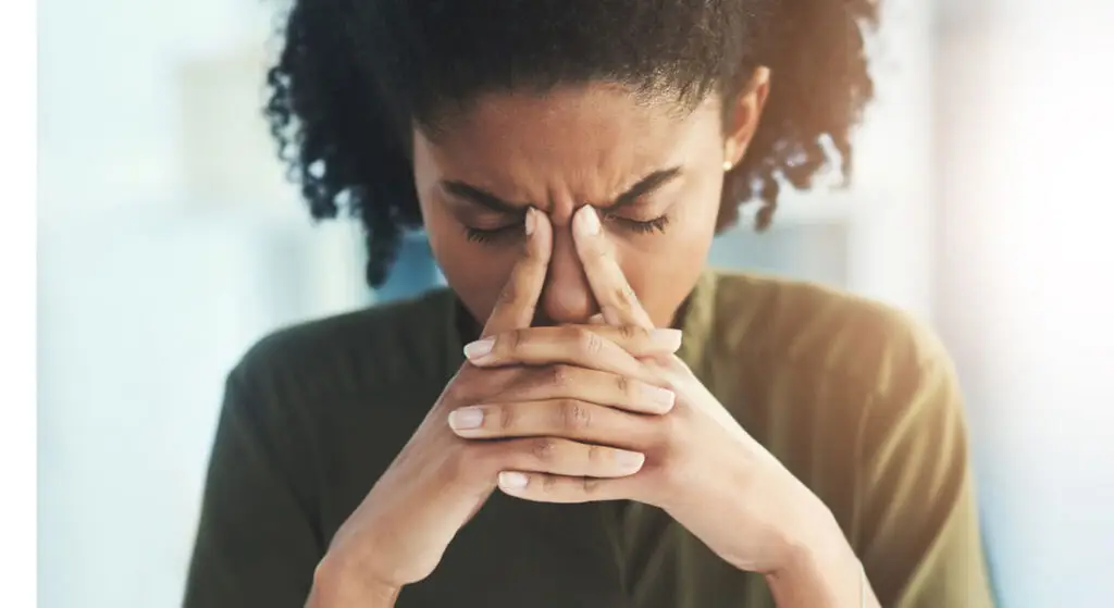 Person with eyes closed, fingers pressed to the forehead in a stressed, contemplative pose.
