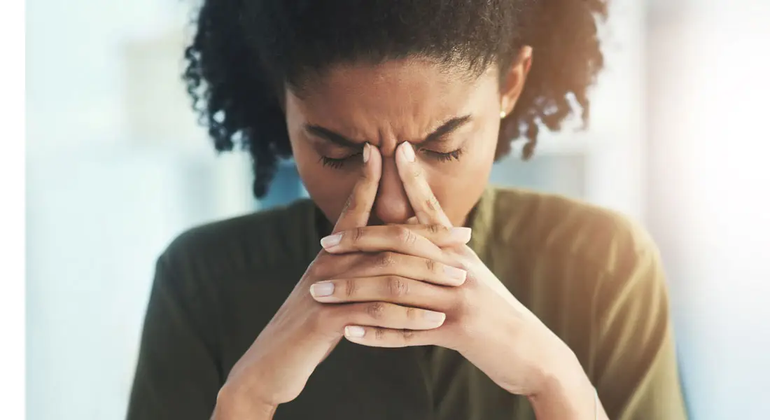 Person with eyes closed, fingers pressed to the forehead in a stressed, contemplative pose.