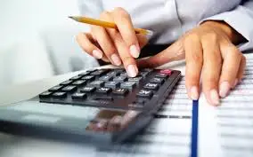Close-up of hands using a calculator and pencil over financial documents and notebook. They appear to be doing accounting or budgeting work.