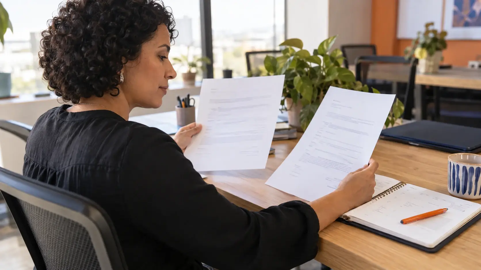 Profissional compara duas propostas e um planejamento anual em uma mesa de trabalho.